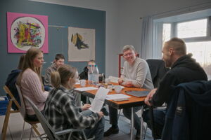 An einem Tisch sitzen 5 Jugendliche und zwei Erwachsene. Sie diskutieren mit sichtlicher Freude über ein Thema. Manche lachen.