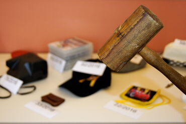 Das Foto zeigt im Vordergrund einen Zuschlagshamme, im Hintergrund eine Reihe von Fundgegenständen.