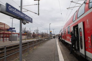 Das Foto zeigt einen rot-weißen Zug. Es steigen Menschen aus und ein. Auf einem Schild steht "Cottbuser Bahnhof".