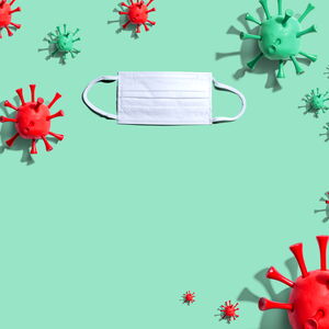 Das Foto zeigt auf grünem Hintergrund grüne und rote Modelle des Corona-Virus und eine OP-Maske.