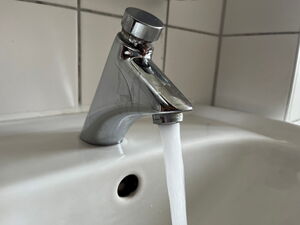 Aus einem silbernen Wasserhahn fließt helles Leitungswasser.