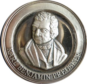 Das Foto zeigt eine Medialle mit dem Portrait eines älteren Herrn. Auf dem Medaillenrand steht seine Name: Karl Benjamin Preusker.