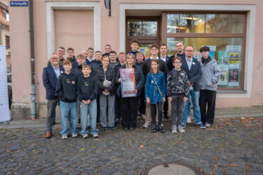 Auf einem Foto steht eine Gruppe von Menschen. Es sind Jugendliche und Erwachsene. Sie lachen in die Kamera.