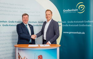 Zwei Männer in Anzügen geben sich die Hand. Sie lächeln in die Kamera.