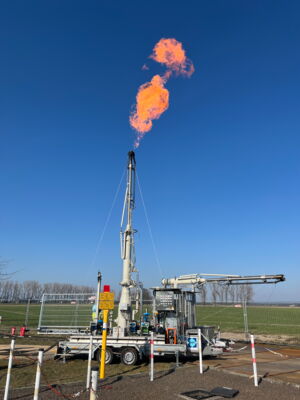 Auf einem Anhänger sieht man technische, silberfarbene Aufbauten. Ein langes Rohr ragt aus diesen heraus. Daraus entweicht eine Flamme.