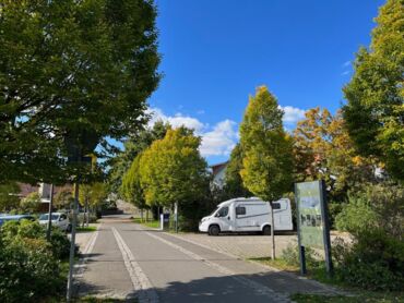 Das Foto zeigte einen Parkplatz, umgeben von vielen Bäumen. Auf der rechten Seite sieht man ein Wohnmobil.