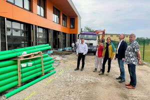 Auf einer Baustelle stehen 5 Menschen, vier Männer und eine Frau. Sie schauen sich die Baustelle an.