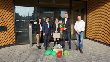 Das Foto zeigt fünf Menschen, zwei Frauen und drei Männer, vor dem Eingang einer Kita. Sie lachen in die Kamera.