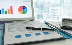 Foto von einem geöffneten Laptop und einen aufgeschlagenen Ringordner. Auf beiden sieht man verschiedene Diagramme.