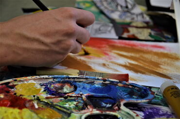 Das Foto zeigt eine Hand, die einen Pinsel hält. Sie mischt Farbe auf eine Farb-Palette.