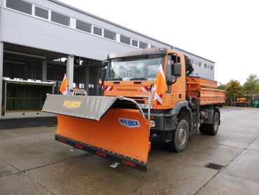 Das Foto zeigt ein orangefarbenes Fahrzeug mit Schiebeschild. Im Hintergrund sieht man das Bauhofgelände.