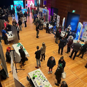 In einem großen Raum stehen viele Messestände, an denen sich Besucher informieren.