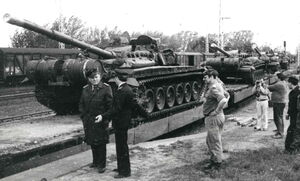 Auf einem schwarz-weiß Foto sieht man mehrere Panzer. Davor stehen Männer in Uniform, die miteinander sprechen.