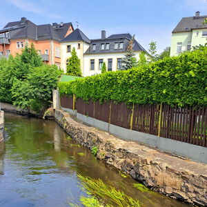 Entlang des Flusses Röder sieht man Uferwänder mit Zäunen und dahinter eine innerstädtische Bebauung mit Mehrfamilienhäusern.