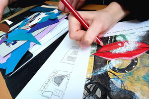 Man sieht bunt ausgemalte Bilder, Skizzen und Ausschnitte übereinander liegen. Jemand mal an einem Bild. Von dem Künstler ist nur die Hand zu sehen, die einen roten Buntstift hält.