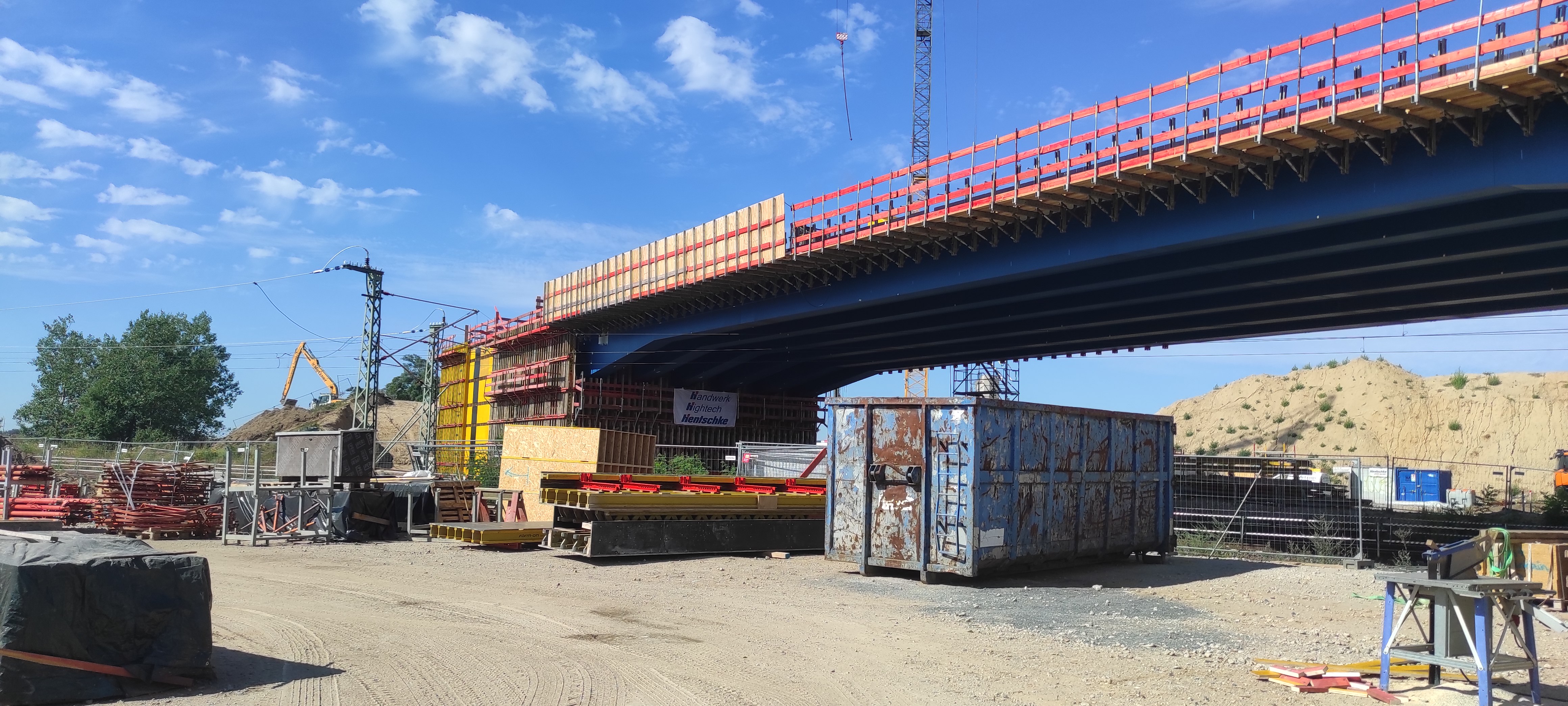 Eine großen Brückekonstruktion dominiert das Bild. Man sieht Container und Fahrzeuhe der Baustelle.