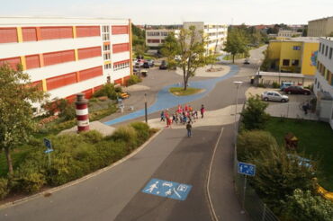 Das Foto zeigt den farbenfrohen Kinderboulevard "Am Schacht". Zu sehen sind ein Leuchtturm und eine Kindergruppe, die die Spielstraße überquert.