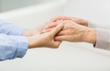 Das Foto zeigt zwei Hände. Eine junge Hand, rechts, hält zwei ältere Hände, links.