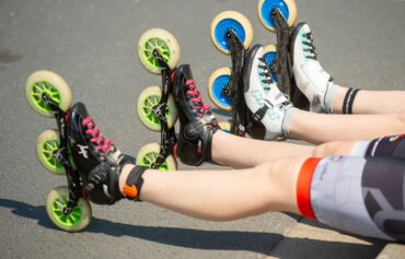 Das Menschen die am Straßenrand sitzen. Man sieht nur ihre Beine. Sie tragen Inline-Skater.